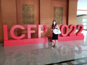 Anna standing in front of a sign that says ICFP 2022 while holding a tote bag