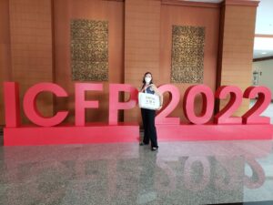 Devon standing in front of a sign that says ICFP 2022 while holding a tote bag
