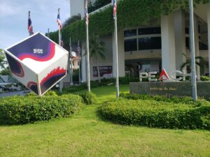 Large cube that says "ICFP 2022" logo in front of conference building on grass