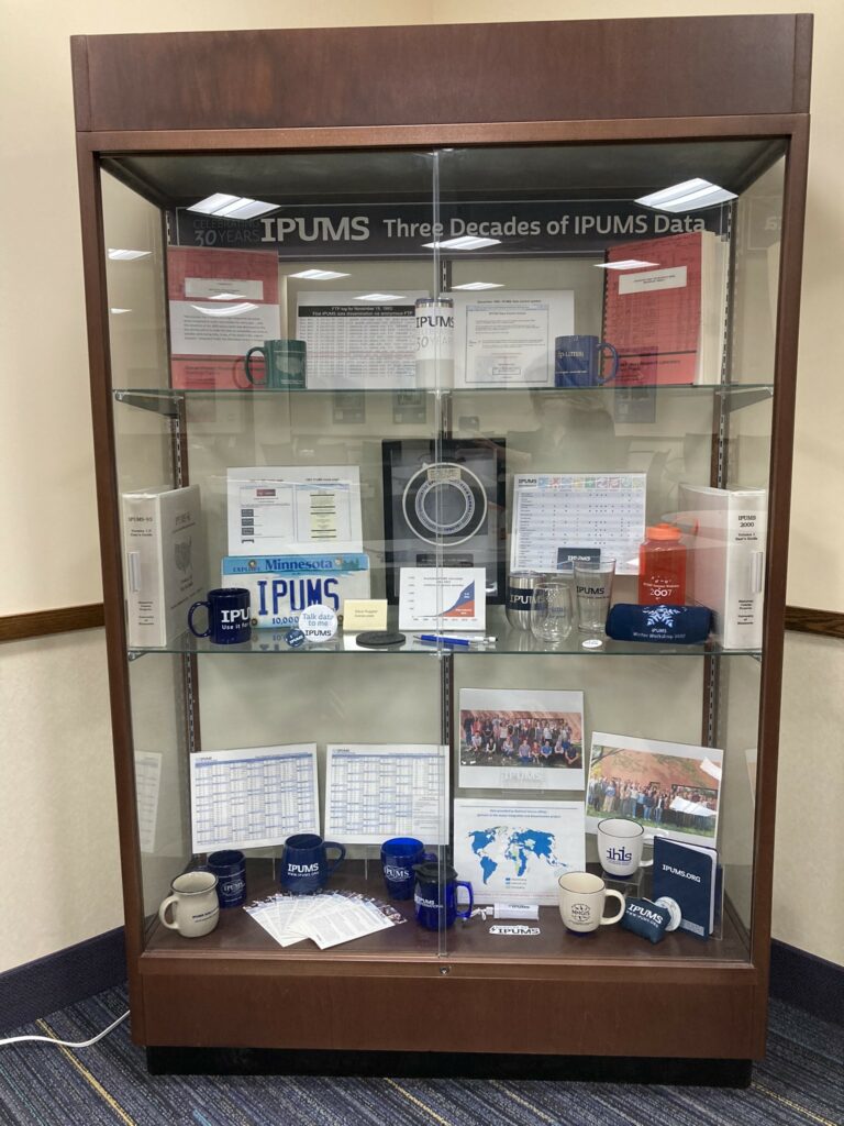 "Celebrating 30 years: three decades of IPUMS data" display case with promotional materials, swag items, and historical IPUMS items